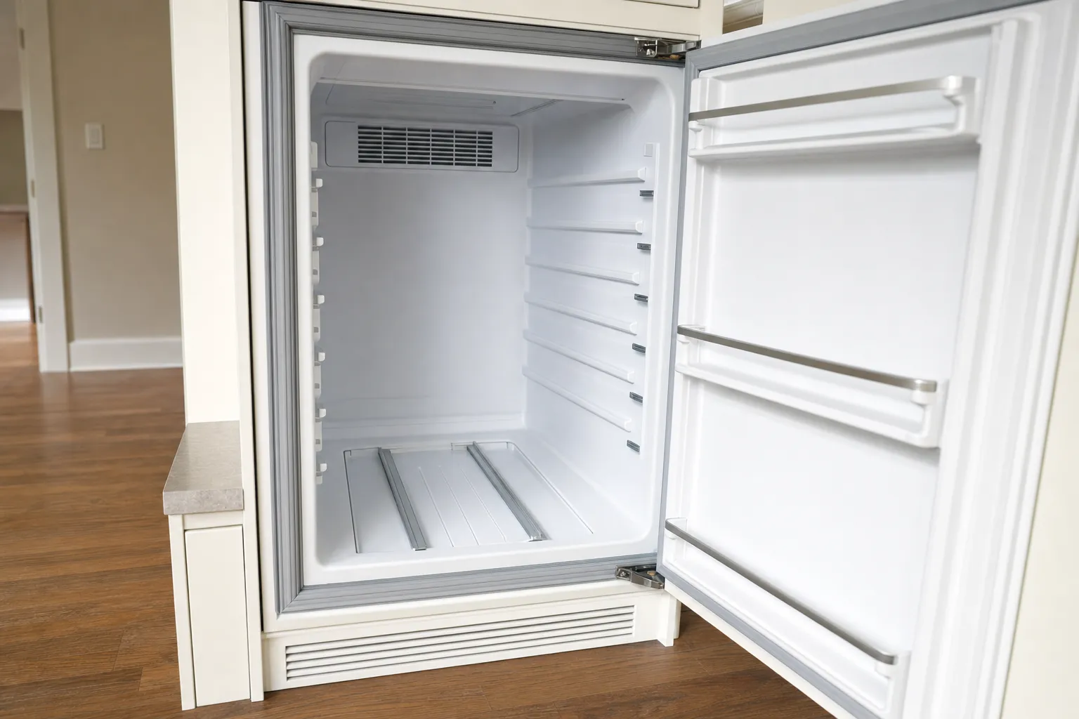 Emptied built-in refrigerator compartment in cream cabinetry, a fan grille across the top of the back wall and a toe-kick vent below